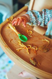 die Hand eines Kindes, welches gerade Spaghetti gegessen hat. Das Essbrett des Hochstuhls ist noch voller Essensreste.